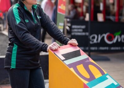 A woman stood leaning on a wooden box which says Listen on it. She is wearing headphones.