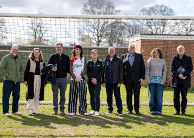A group of people stood in a line smiling at the camera. They are in front of a football goal on a grass pitch.