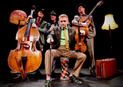 Group portrait of musicians with violin, accordion, guitar and double bass, seated and standing together against a dark backdrop in smart concert attire