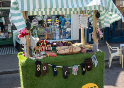 Grass carpeted stall featuring a black and yellow logo titled ZEST. The stall is filled with fruits, dolls and gloves