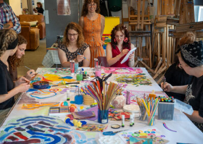 Group of people painting, there are bright colours around the room and table